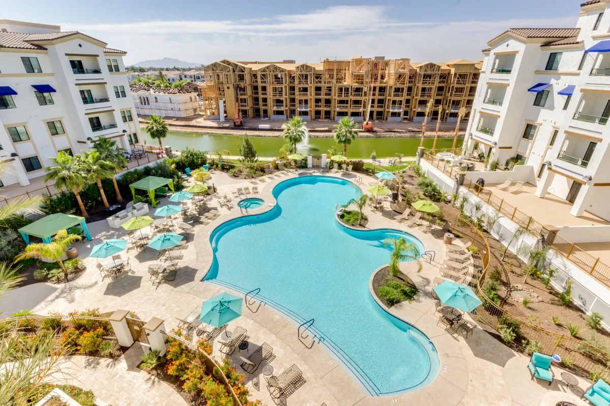 A beautifully landscaped pool area featuring a large, heated swimming pool surrounded by lush greenery, resort-style lounge chairs, and several cabana areas. The tranquil atmosphere is ideal for both relaxation and socializing, with ample space for sunbathing or enjoying a morning coffee by the water.