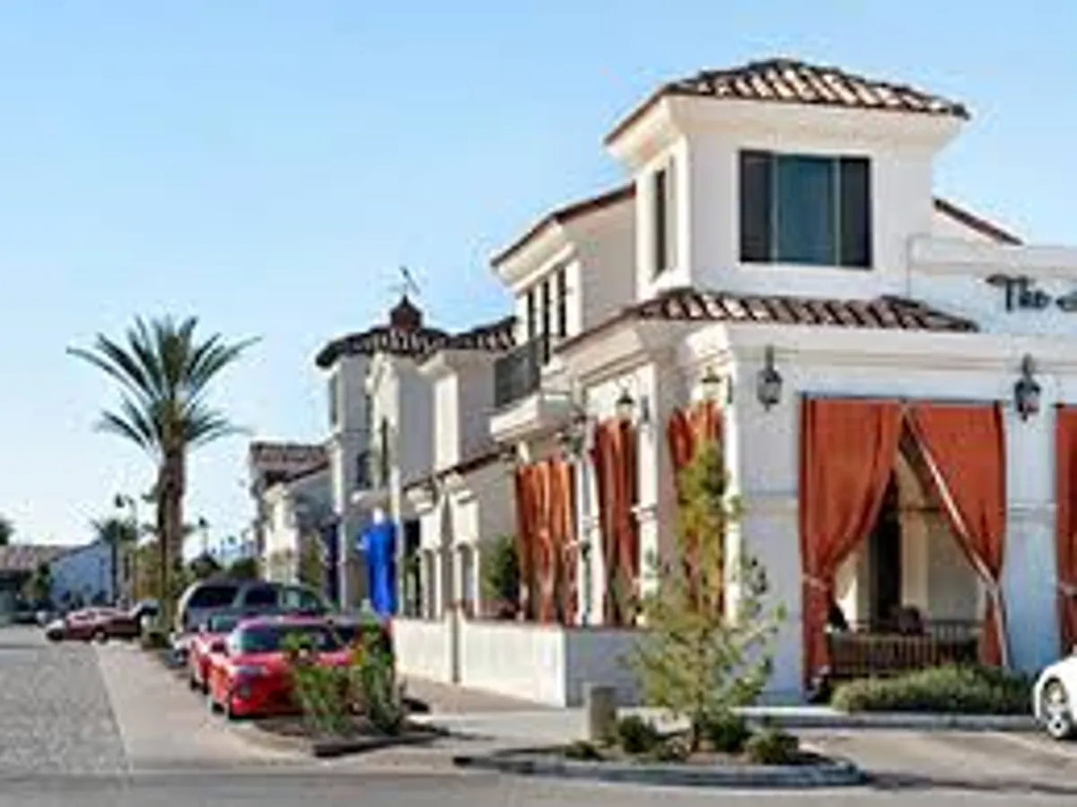 An inviting exterior facade of an elegant building with large windows, colorful cars parked outside, and decorative curtains. The scene hints at accessible shops, cafes, and potential patio seating, capturing the essence of neighborhood convenience and charm.