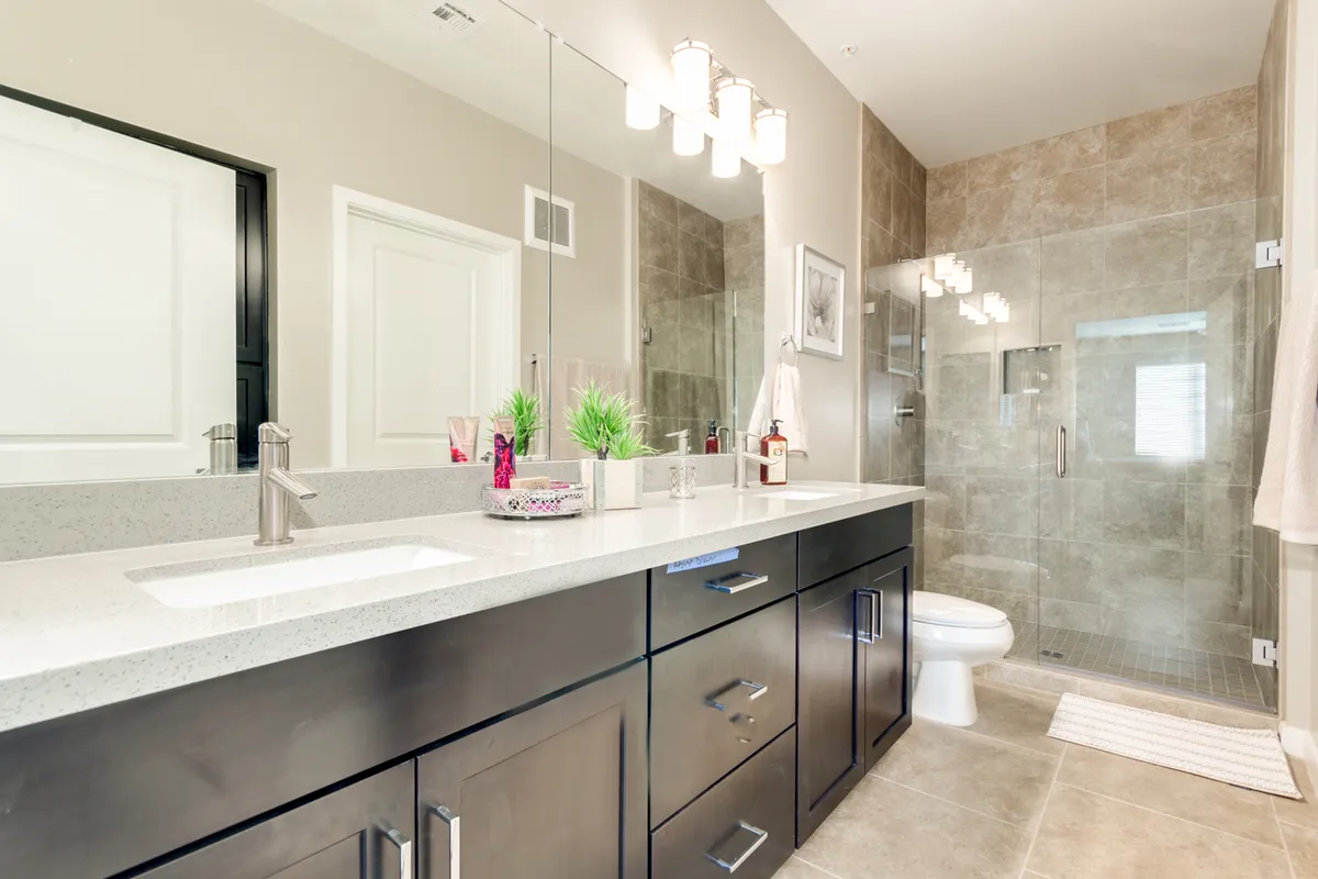 A modern bathroom featuring a double vanity sink, glass shower enclosure, and stylish light fixtures. The space is bright and fresh, suggesting an updated and spa-inspired atmosphere.