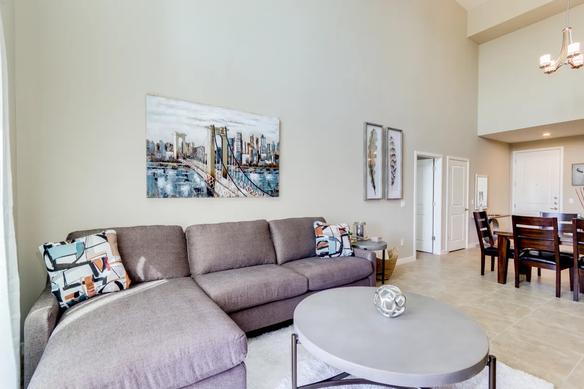 A comfortable and modern great room featuring a large sectional sofa, contemporary artwork, a sleek coffee table, and a dining area for six. The space flows seamlessly, offering ample seating and a welcoming atmosphere for socializing, relaxing, or entertaining guests.