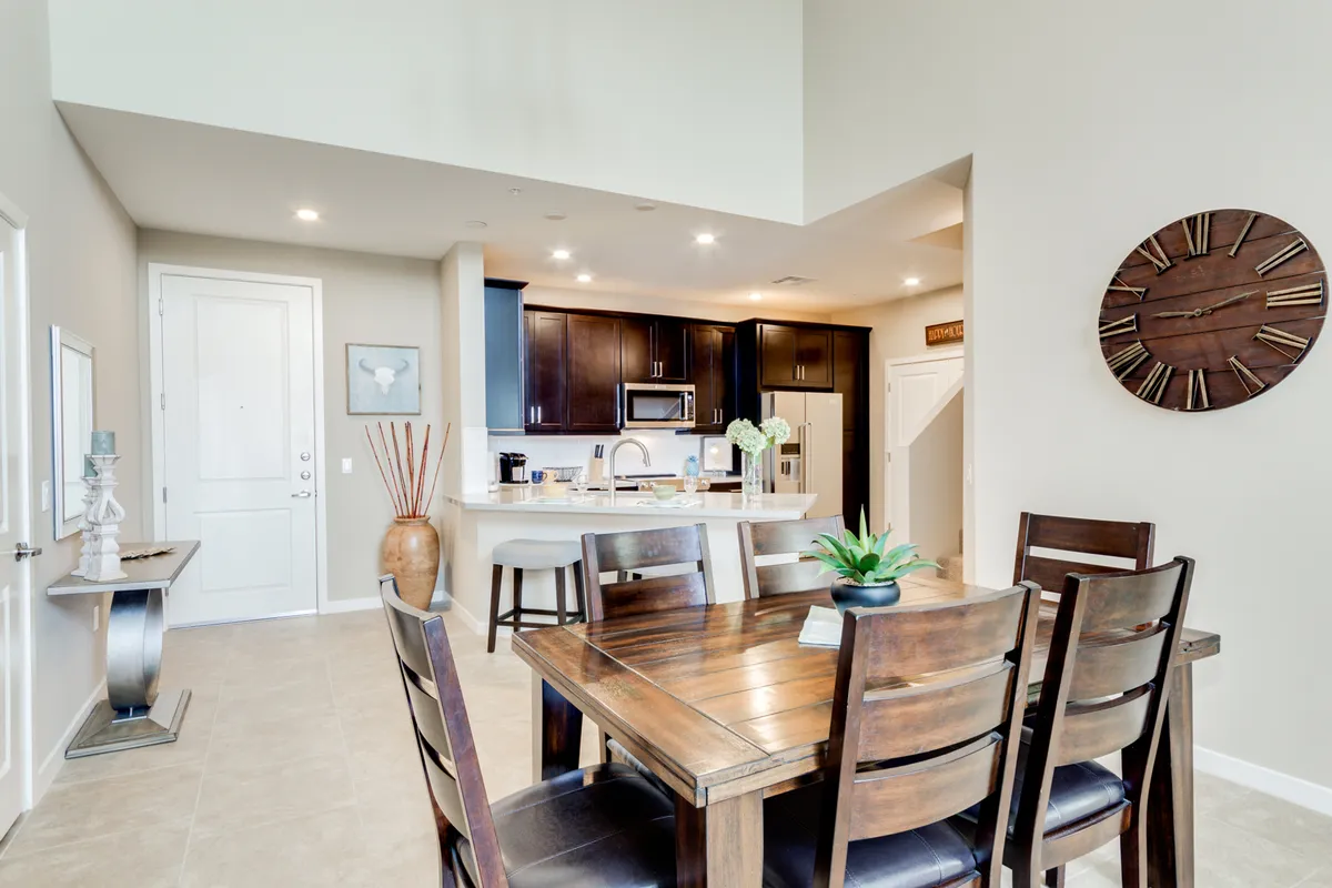 A welcoming dining area adjacent to the kitchen, featuring a large table set for family meals, a kitchen island in view, a decorative vase, and a wall clock. The setting is staged for family dinners or entertaining guests, reinforcing the kitchen's connection to communal dining experiences.