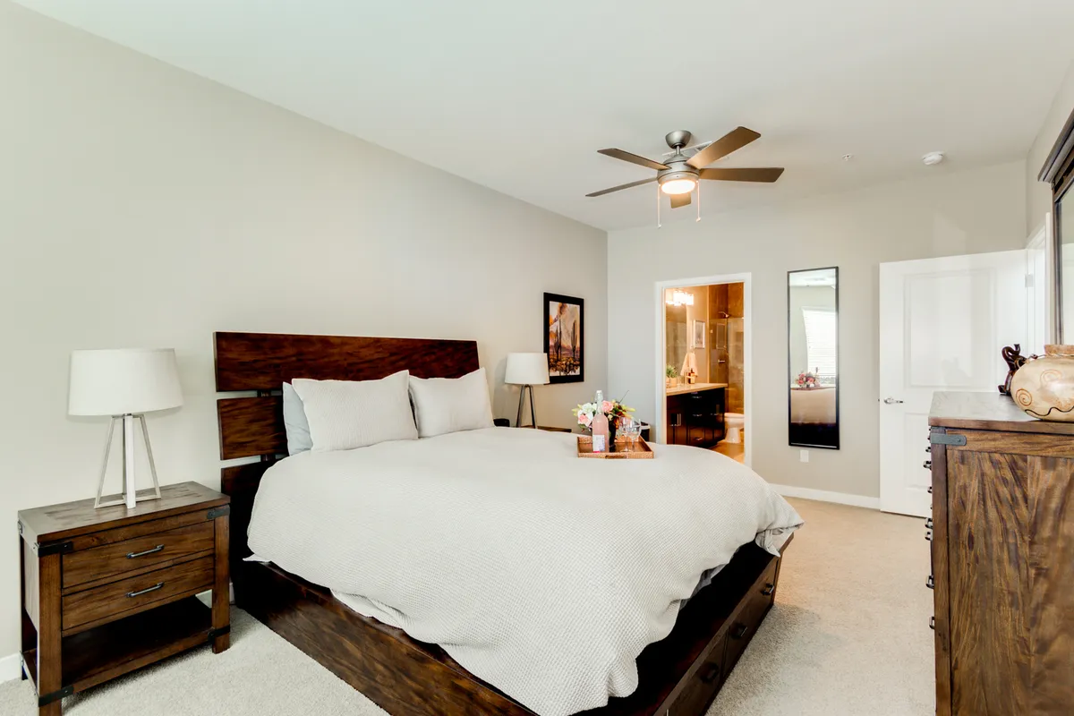 This image showcases a serene bedroom, featuring a neatly made bed flanked by nightstands, soft artwork, and a wall mirror. The overall mood is calm and inviting, perfect for restful nights and quiet moments spent reading or relaxing.